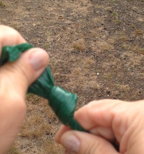 Hands tying a knot in a green waste bag